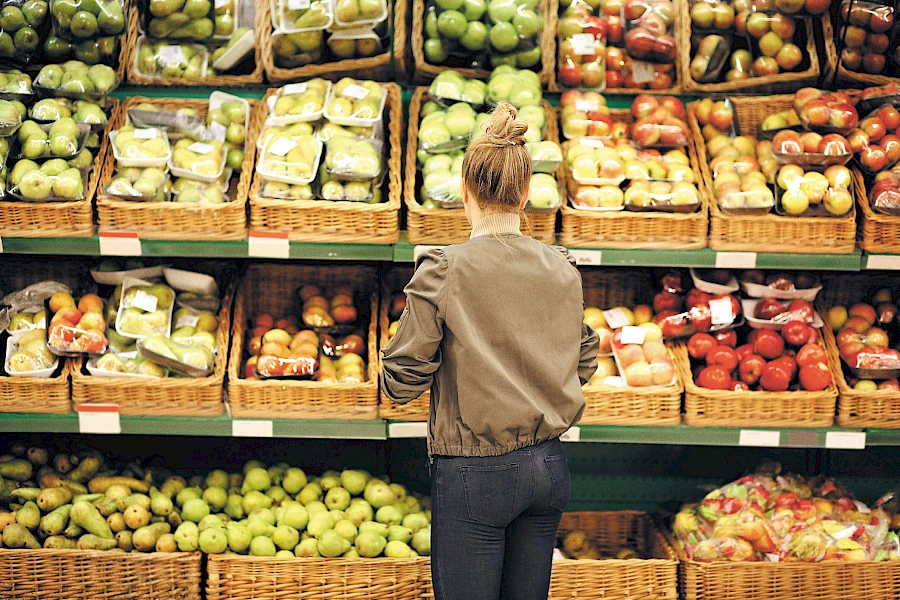 Eine Person steht vor einem gut gefüllten Obstregal und schaut sich die Waren und Preise an.